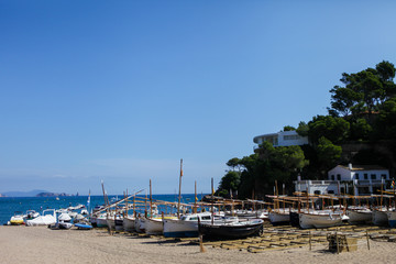 Fototapeta na wymiar Traditional fishing boats standing in the shore. Small fisherman's village in Catalonia, Spain. Wooden boats on the bay, Mediterranean sea. White buildings are on the background. Summer vacations