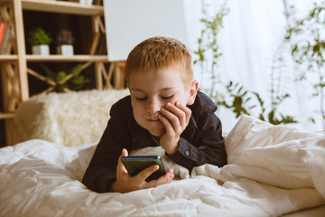 Boy using different gadgets at home. Little model with smart watches, smartphone or tablet and headphones. Making selfie, chating, gaming, watching videos. Interaction of kids and modern technologies.