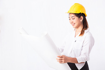 Beautiful young Asian woman wearing yellow safety helmet. Architect woman looking blueprint paper and smiling while standing at her working place with white background and copy space.