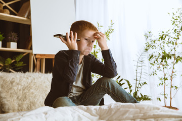 Boy using different gadgets at home. Little model with smart watches, smartphone or tablet and headphones. Making selfie, chating, gaming, watching videos. Interaction of kids and modern technologies.