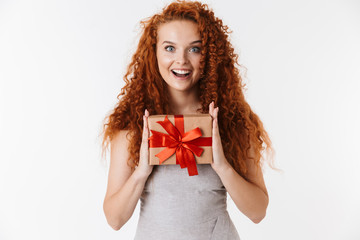 Redhead curly girl isolated over white wall background holding surprise box gift.