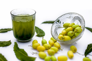 Detox or detoxifying drink of neem fruit in a glass isolated on white along with some neem fruit or...