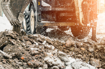 digging the earth in winter. Tractor works on the construction site in the cold winter Construction and snow removal equipment at the plant - loader with snow unloading during roadworks