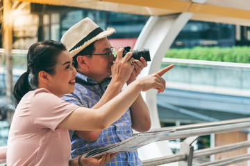 Asian couple retirement age,  tourists are happy With photography Various tourist attractions By looking at the map That the wife holds in her hand, to travel and elderly concept.
