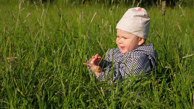 Little baby girl sitting in tall grass, counting on fingers, then look away. Tiny kid have fun, enjoy nature outdoors, play some game.