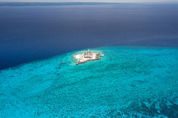 Aerial drone view of a lighthouse on a tiny tropical island surrounded by coral reef and deep water (Capitancillo Island, Cebu, Philippines)