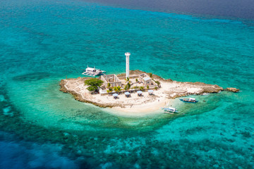 Aerial drone view of a lighthouse on a tiny tropical island surrounded by coral reef and deep water...