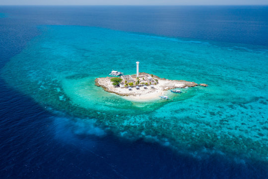 Aerial drone view of a lighthouse on a tiny tropical island surrounded by coral reef and deep water (Capitancillo Island, Cebu, Philippines)