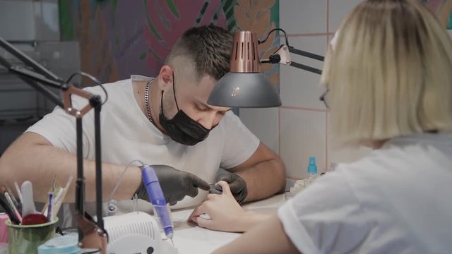 Professional manicurist man removes cuticles with special scissors.