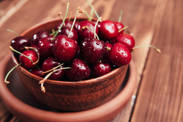 ripe sweet cherry in an earthenware dish on a wooden background