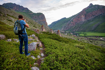 Male hiker takes photo of beautiful mountains and ancient tombs. North Caucasus