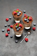 Classic tiramisu dessert with blueberries and raspberries in a glass on dark concrete background