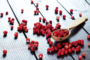 Wild strawberry in a wooden spoon cup on wooden table with forest berry scattering around, closeup, copy space, healthy food and vegetarian eating concept