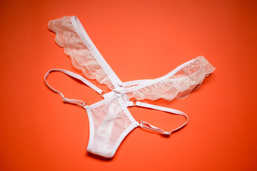 White lace panties on a coral background. Female underwear for the bride on an orange background.