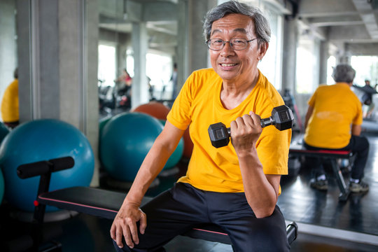 Senior asian sport man lifting dumbbells in fitness gym . elder male exercising ,  working out , training weights, healthy ,Retirement , older, looking camera