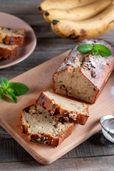 Banana sweet bread sliced on a wooden cutting board with bananas in background