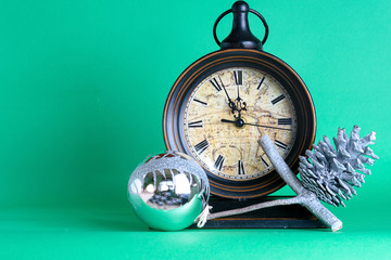 New Year's clock, bauble and cone on pine fir tree branch. Green background. Christmas greeting card.