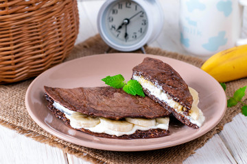 Chocolate pancake from oatmeal with banana and cheese on a wooden background