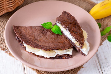 Chocolate pancake from oatmeal with banana and cheese on a wooden background