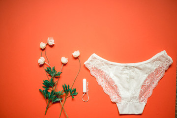 White lace panties with tampon on a coral background. Female underwear for the bride with delicate flowers on an orange background.