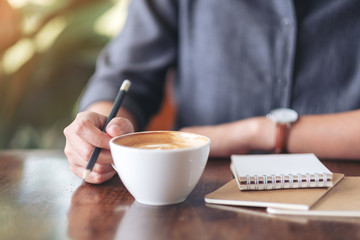 Fototapeta na wymiar Closeup image of a woman writing on blank notebook while drinking coffee