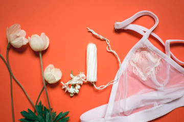 White lace bra with tampon on a coral background. Female underwear for the bride with delicate flowers on an orange background.