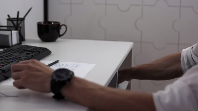 Detective is playing fifteen puzzle tag for rest on his workplace thinking about complicated case, hands closeup. Man is sitting at table in office and playing board game.