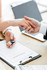 cropped view of woman holding keys in hand and shaking hands with realtor