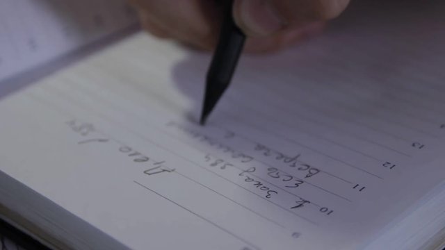 Detective makes a plan of work of the case. Closeup of man's hands is writing a checklist for work in his diary on russian language.
