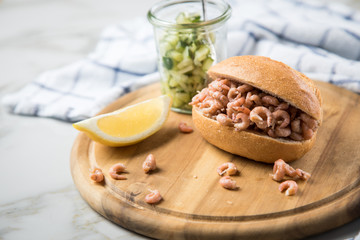 Nordseekrabben Brötchen als Fischbrötchen mit Gurkensalat und Zitrone auf Holz Brett und Marmor...