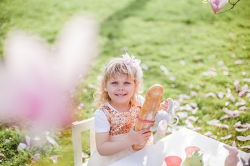 Two cute little blonde girls of 3 years old are playing in the park near a blossoming magnolia. Tea drinking. Easter.