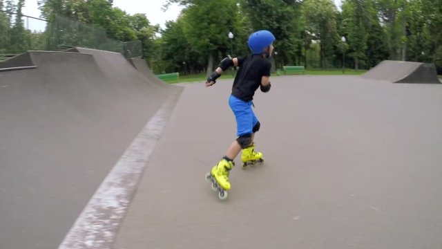 Athletic schoolboy leisure. Kid on rollerblades skating on the ramp in the park