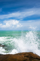 Relaxing ocean waves crashing into rocky shore on sunny summer.