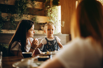 An attractive mother and her pretty girl, together with her girlfriend, rest in the cafe at the table, communicate with each other, eat and drink. beautiful woman with a child on holiday at restaurant