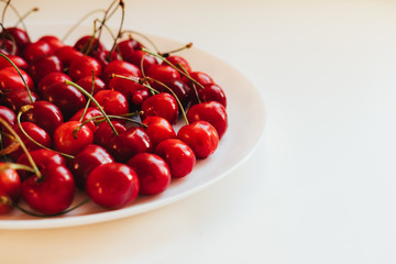 Plate with sweet cherries closeup. Freshly harvested summer berry in white bowl. Vitamin containing ripe fruits. Raw food ingredient, vegetarian diet component. Bio, eco, organic farming produce
