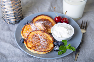 Cottage cheese pancakes (syrniki). Homemade cheesecakes from cottage cheese with sour cream, berries and milk. Traditional Russian dish. Close-up.
