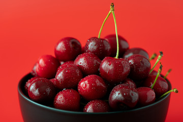 Macro shot of freshly picked cherries in a black ceramic bowl. Bright red background, water drops, high resolution