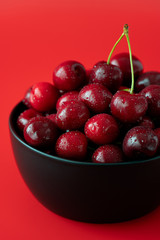 Macro shot of freshly picked cherries in a black ceramic bowl. Bright red background, water drops, high resolution