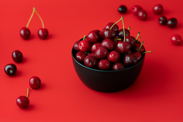 Freshly picked cherries in a black ceramic bowl. Bright red background, water drops, high resolution