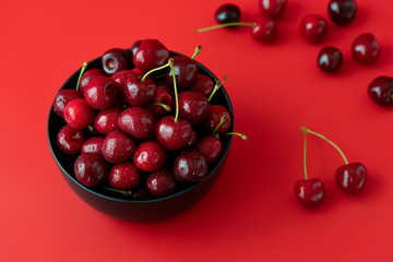 Freshly picked cherries in a black ceramic bowl. Bright red background, water drops, high resolution