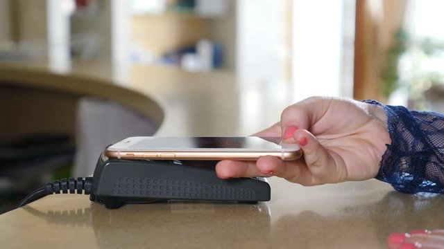 Female paying with smart phone using NFC technology. Close-up. Contactless payment with smartphone. Paying with a smartphone device on a credit card terminal. Wireless payment. 4K.