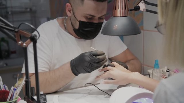 Professional manicurist man varnishes a girl's nails.