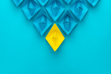 yellow paper ship ahead of blue ones leadership concept over blue background. top view of race with...
