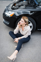 Fototapeta na wymiar beautiful businesswoman talking on smartphone and sitting near broken auto, car insurance concept