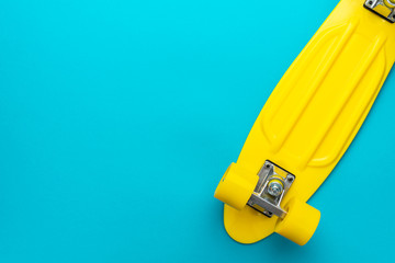 minimalist flat lay photo of yellow plastic mini cruiser board on blue background. top view of bright yellow cruiser skateboard with copy space