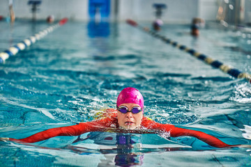 Female athlete in a red-yellow swimsuit is swimming in the style of breaststroke. Splashes of water...