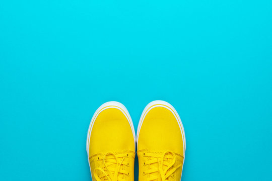 Minimalist photo of yellow sneakers with tied shoelaces. Flat lay image of yellow summer footwear. Pair of yellow sneakers on turquoise blue background. Top view of skateboarding shoes with copy space