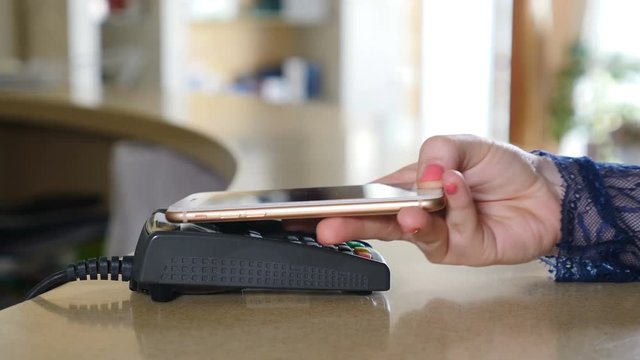 Female customer paying with smart phone using NFC technology. Close-up. Contactless payment with smartphone. Paying with a smartphone device on a credit card terminal. Wireless payment. 4K.