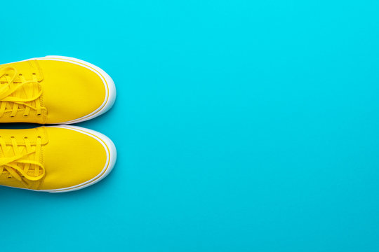 Top view of skateboarding shoes with copy space. Pair of yellow sneakers on turquoise blue background. Minimalist photo of yellow sneakers with tied shoelaces. Flat lay image of yellow summer footwear