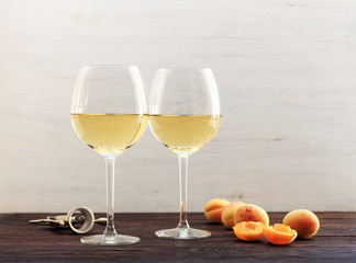 Apricots and two glasses of the white wine, on a wooden background.